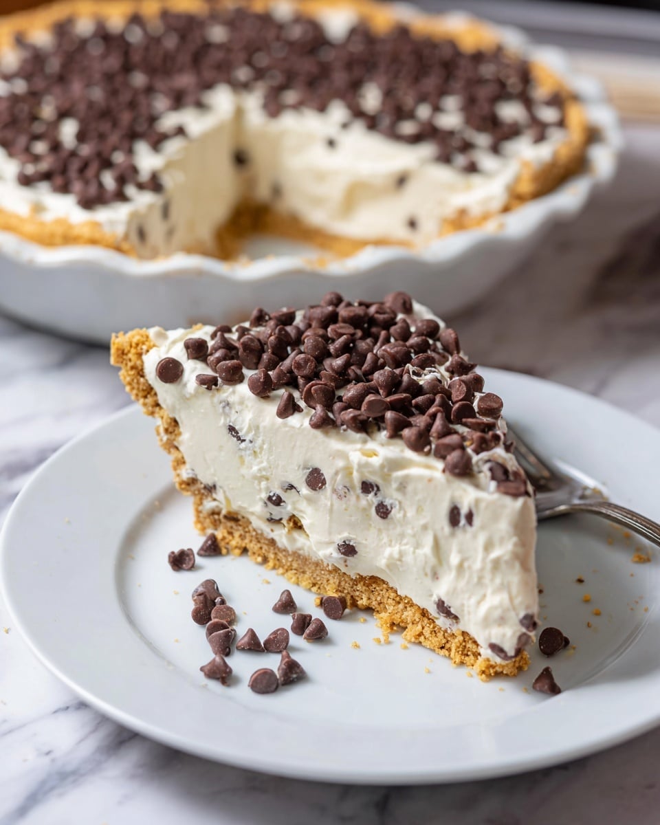 A slice of creamy pie sits on a white plate, showing three clear layers: a golden brown crumbly crust at the bottom, a thick middle layer of white creamy filling mixed with small chocolate chips, and a top layer of smooth white cream sprinkled heavily with mini chocolate chips. A silver fork rests beside the slice, and a few chocolate chips are scattered around the plate. In the background, the full pie is visible in a white pie dish, with the same creamy and chocolate chip topping and golden crust. The surface is white with a marbled texture. photo taken with an iphone --ar 4:5 --v 7