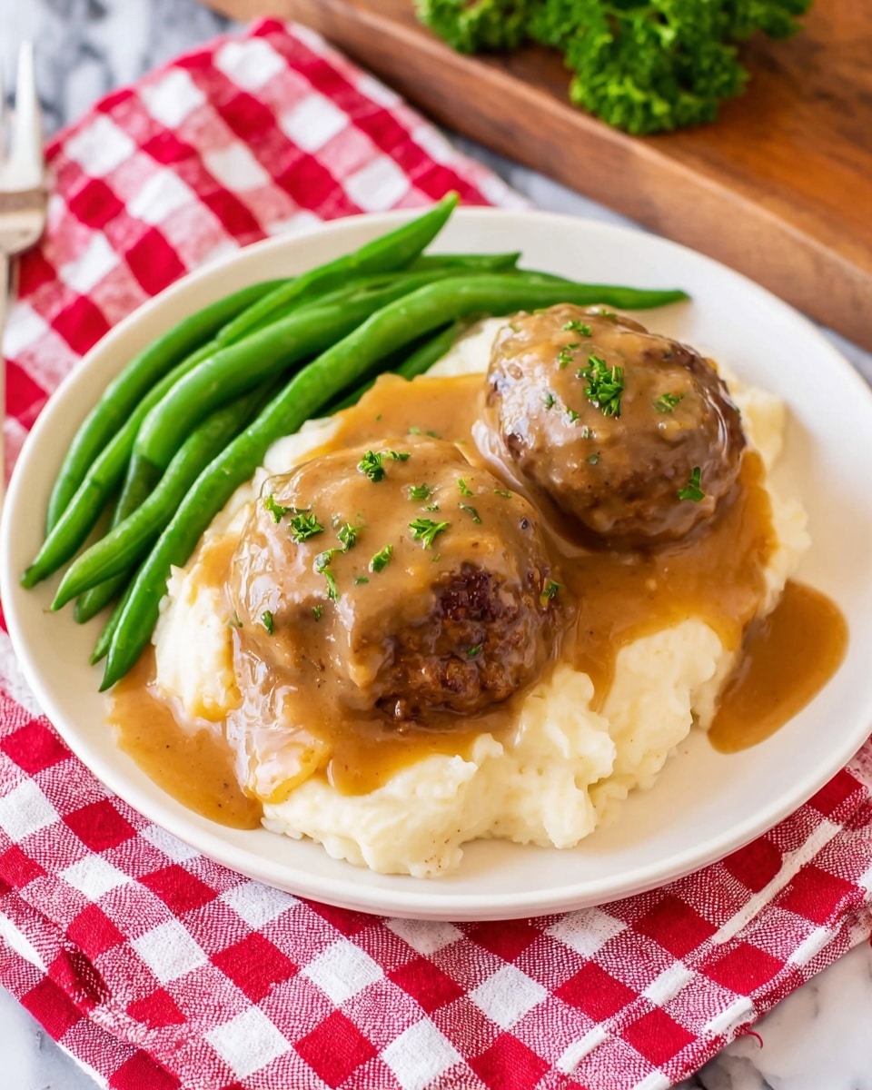 A white plate holds three main layers: at the bottom is a smooth, creamy layer of mashed potatoes with a soft, light beige color and slightly textured surface; on top of this are two rounded meat patties, dark brown with seared edges, covered thickly with a shiny, golden-brown gravy sauce that drips slightly down the sides; small green parsley pieces are sprinkled over the gravy for a fresh touch; on the left side of the plate is a pile of bright green, firm green beans with a smooth texture. The plate is set on a red-and-white checkered cloth, resting on a white marbled surface. photo taken with an iphone --ar 4:5 --v 7
