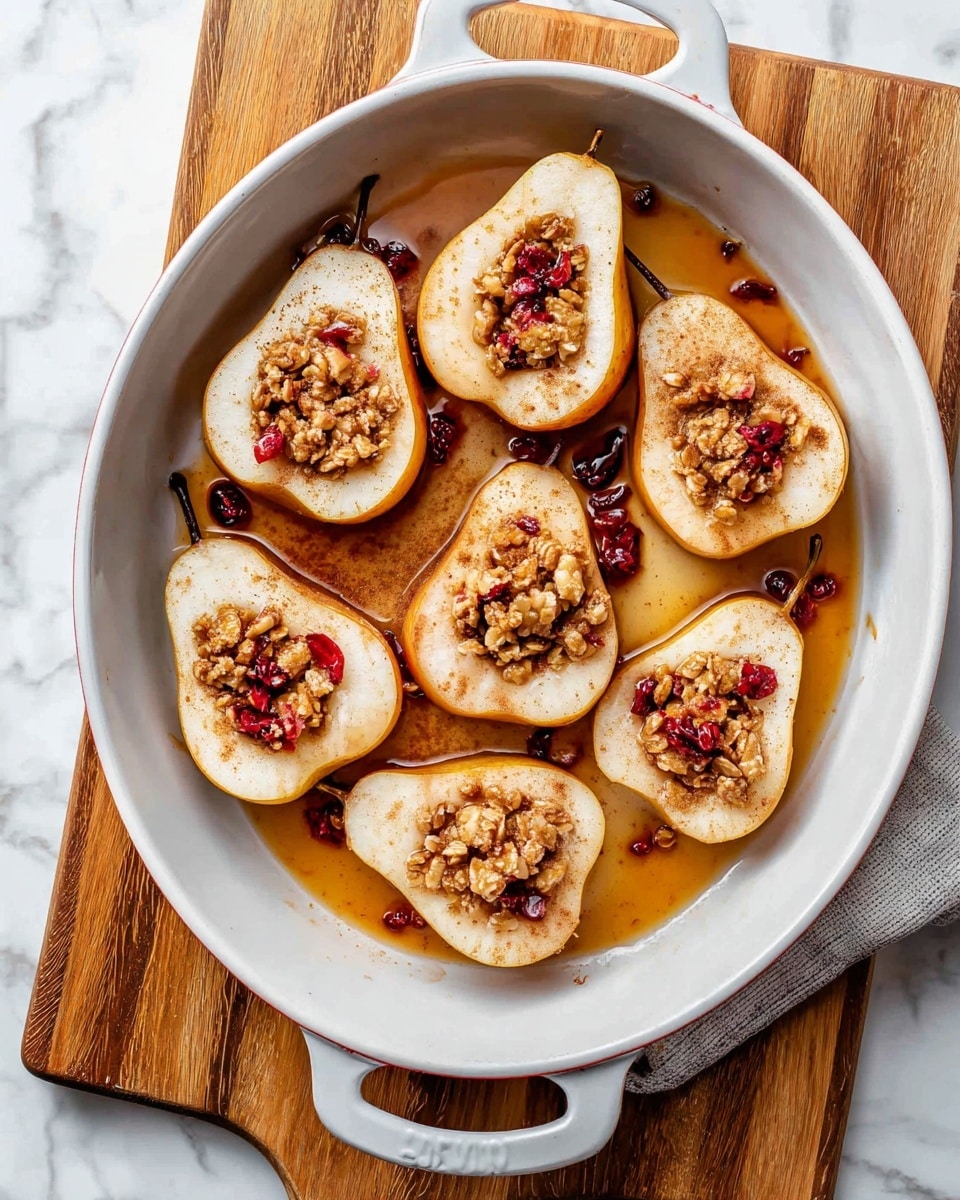 The image shows eight pear halves arranged in a round white baking dish with two handles. Each pear half is cut lengthwise and placed with the cut side facing up, revealing a hollow center filled with chunky brown granola and small bits of red berries. The pears are light cream-colored with a warm golden tint near the edges, and they are sprinkled with a light dusting of cinnamon powder. Surrounding the pears is a thin layer of amber-colored syrup that pools slightly at the bottom of the dish. The baking dish sits on a wooden cutting board, all set on a white marbled surface. Photo taken with an iphone --ar 4:5 --v 7