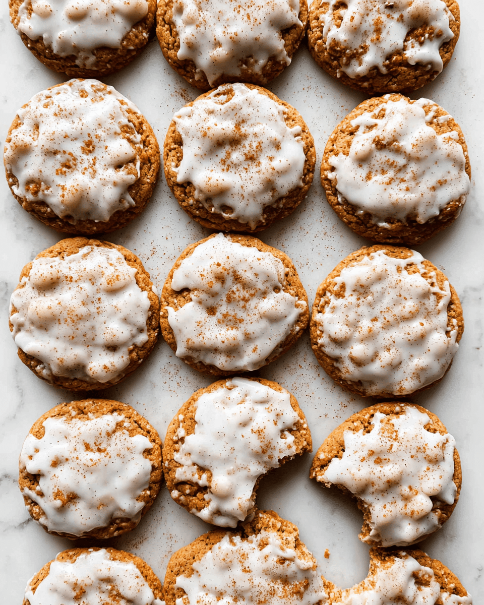 The image shows fifteen round cookies arranged closely together on a white marbled surface. Each cookie has one thick layer of light brown base with a rough, slightly crumbly texture, topped with an uneven layer of white icing that is spread irregularly, creating patches and drips, with a light dusting of brown cinnamon powder sprinkled on top. One cookie on the right has a visible bite taken out of it, revealing the moist interior. The overall look is warm and homemade. photo taken with an iphone --ar 4:5 --v 7