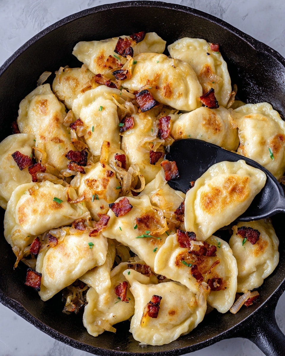 This image shows a black cast iron pan filled with golden brown pierogies, each piece half-moon shaped with a soft, smooth dough texture. The pierogies are lightly browned on some sides, with bits of crispy, dark reddish-brown bacon pieces and caramelized yellow onions scattered on top and mixed in. A black serving spoon rests in the pan, lifting one pierogi. The pan sits on a white marbled surface. photo taken with an iphone --ar 4:5 --v 7
