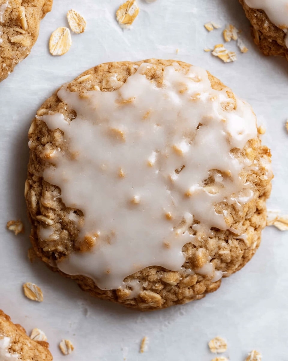 A close-up view of one oatmeal cookie covered with a smooth white glaze that lightly drips over the edges. The cookie itself has a golden brown color with a rough, uneven texture showing oats embedded in the dough. Small oat flakes are scattered around the cookie on a white marbled textured surface. The glaze layer covers the top fully but is thin enough to see some of the cookie's texture through it. photo taken with an iphone --ar 4:5 --v 7