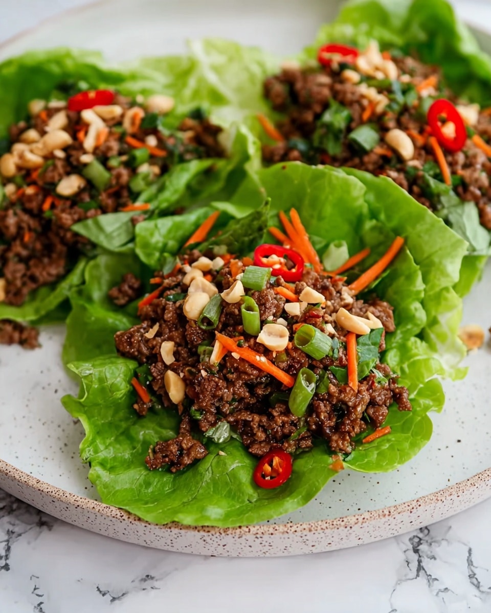 The image shows three lettuce wraps placed on a white plate with a white marbled surface underneath. Each wrap is made with a large green lettuce leaf as the base, topped with a layer of dark brown cooked ground meat mixed with small pieces of green onions and thin orange carrot strips. The meat is garnished with chopped peanuts and slices of red chili peppers, adding texture and color contrast. The lettuce leaves appear fresh and crisp, with the filling piled in the center, creating a colorful and appetizing look. Photo taken with an iphone --ar 4:5 --v 7