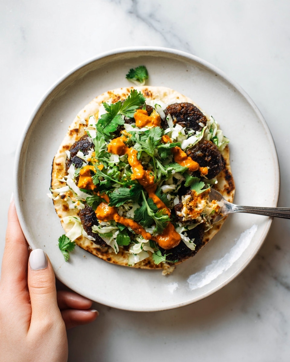 A small round flatbread sits on a white plate, held by a woman's hand at the lower right edge. The flatbread is topped with a dark brown grilled or fried patty, covered with fresh chopped green herbs and white cabbage pieces, giving a mix of green and white textured layers above the patty. On top, a spoon held above spreads thick orange sauce in dollops across the herbs. The background is a clean white marbled texture. photo taken with an iphone --ar 4:5 --v 7
