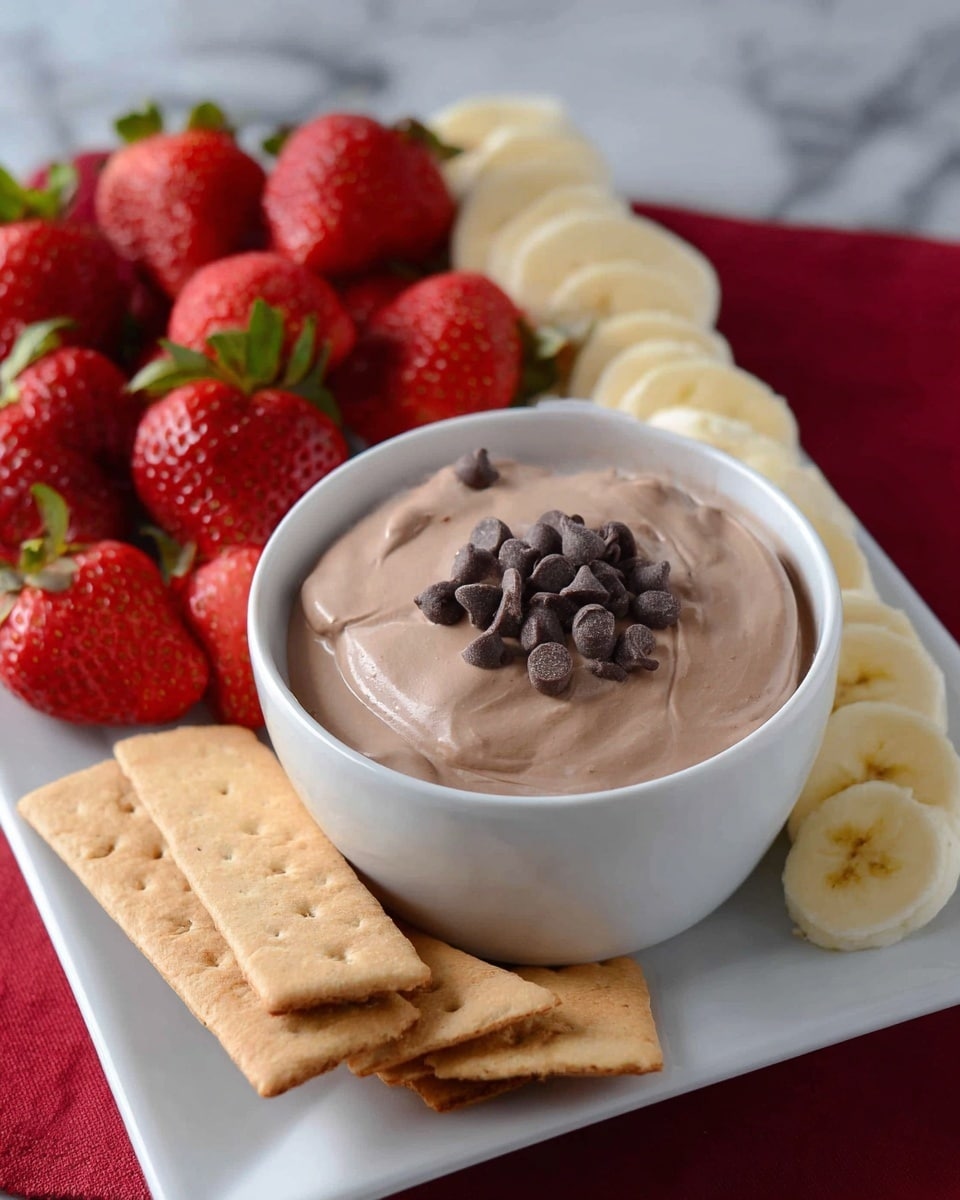 A white bowl filled with smooth, creamy light brown chocolate dip topped with a small pile of dark chocolate chips sits in the center of a white rectangular plate. To the left of the bowl, there is a layer of bright red whole strawberries with green leafy tops, and behind them a layer of pale yellow banana slices. To the right of the bowl, there are several light brown rectangular graham crackers stacked slightly overlapping. The white rectangular plate is on a white marbled surface with a red cloth partially visible in the background. photo taken with an iphone --ar 4:5 --v 7
