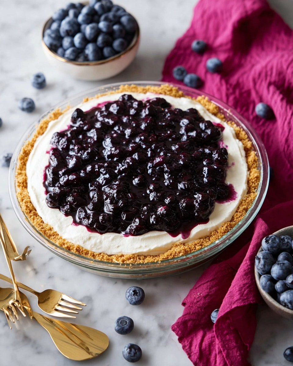 A round pie with three visible layers is shown on a white marbled surface. The bottom layer is a golden brown crumb crust, slightly thick and evenly pressed against the edges of a clear glass pie dish. Above the crust is a smooth, thick white cream layer, spread evenly but with soft peaks around the edge. The top layer is a glossy, dark purple blueberry topping made of whole blueberries and jam, generously covering the cream and slightly spilling over the sides. Around the pie are scattered fresh blueberries, a bowl filled to the top with blueberries, two gold forks resting on a bright magenta cloth, and a gold serving spatula with a branch-like handle. Photo taken with an iphone --ar 4:5 --v 7