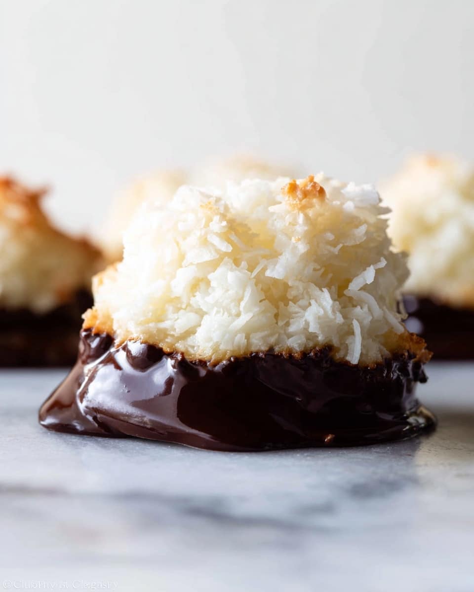 A close-up image of a coconut macaroon showing two layers: the top layer is a mound of rough, white shredded coconut with a slightly textured surface, while the bottom layer is smooth, shiny dark chocolate coating that partially surrounds the base, creating a dripping effect on a flat light surface with a white marbled texture in the blurred background photo taken with an iphone --ar 4:5 --v 7