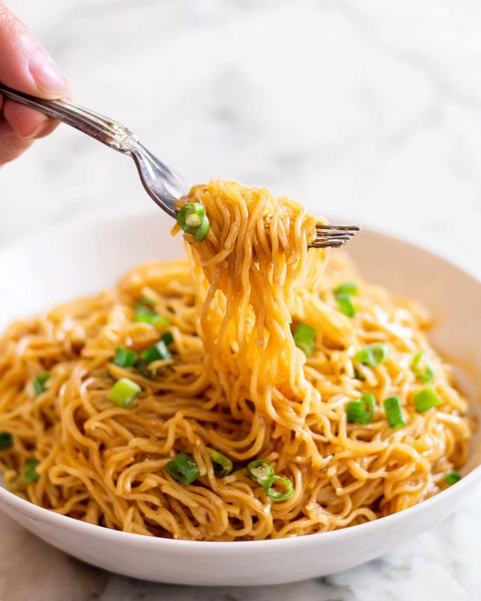 A white bowl filled with cooked thin noodles that are golden brown from sauce, topped with small pieces of bright green chopped scallions scattered evenly. A fork is lifting a small bundle of these noodles from the bowl, showing the shiny and slightly oily texture of the noodles with some scallions stuck to them. The background has a white marbled texture, and a woman's hand is holding the fork from the top right corner of the image. photo taken with an iphone --ar 4:5 --v 7