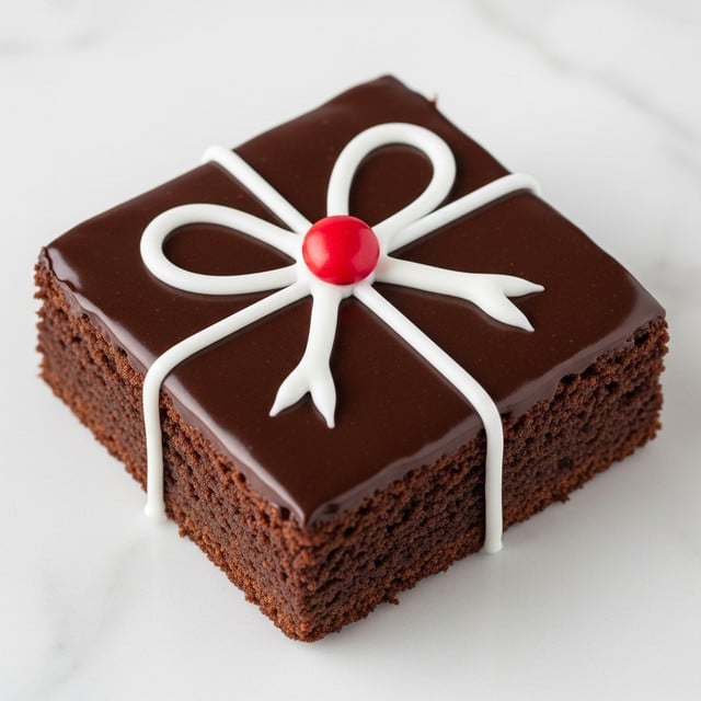 A square chocolate brownie with a smooth, shiny dark brown chocolate glaze covers the top and sides, with slightly rough edges showing the dense cake texture. On top, white icing is piped in the shape of a simple bow, with two large loops and two straight lines crossing in the middle, giving it a wrapped gift look. A single bright red candy sits right at the center of the bow, adding a pop of color. The brownie rests on a white marbled surface. photo taken with an iphone --ar 4:5 --v 7