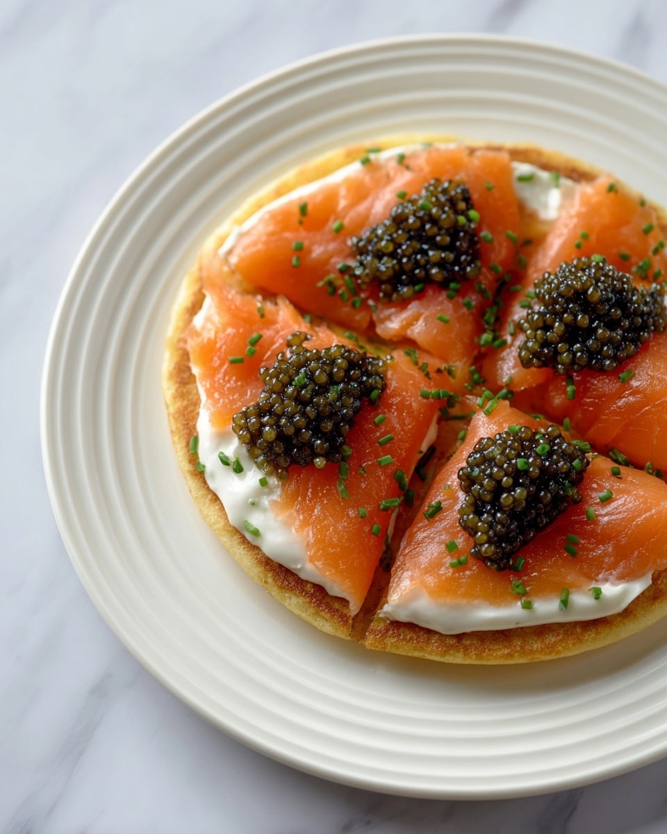 A round, slightly browned pancake base forms the bottom layer, topped with a smooth, white creamy spread. On top of the cream, there are four slices of bright orange smoked salmon, each slice positioned on a quarter of the pancake. Each salmon slice is crowned with a small mound of shiny, black caviar that looks glossy and textured. The dish is finished with sprinkles of finely chopped green chives across the salmon and cream. The food is served on a white plate with ridged edges, all placed on a white marbled surface. photo taken with an iphone --ar 4:5 --v 7