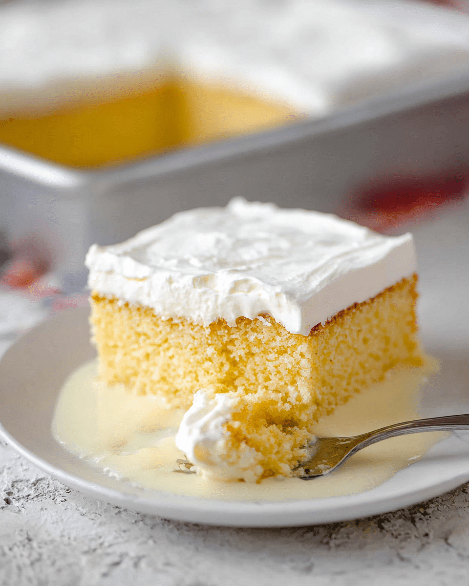 A square piece of yellow sponge cake with a thick, smooth white cream layer on top sits on a white plate, with some creamy liquid pooling around the base of the cake. A silver fork rests on the plate next to the cake, holding a small bite of the cake and cream. In the blurry background, a part of the larger cake in a baking pan is visible. All is placed on a white marbled textured surface. photo taken with an iphone --ar 4:5 --v 7