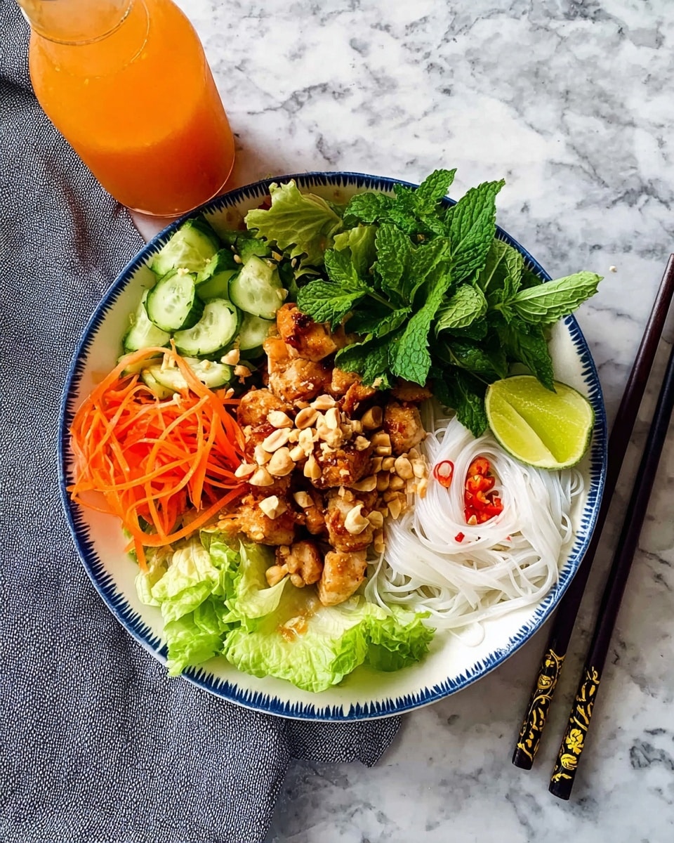 A white bowl with a blue rim holds a colorful layered dish. The bottom layer is white rice noodles on the right, topped with small bits of red chili. Next to the noodles is a layer of light green leaf lettuce. Above the noodles, there is a layer of cooked, golden-brown chicken pieces sprinkled with crushed peanuts and some red chili bits. To the left of the chicken, there is a heap of fresh green cilantro leaves, followed by bright orange shredded carrots. Above the chicken and carrots is a section of light green sliced cucumber and fresh mint leaves. A fresh lime wedge sits on top near the center. The bowl is placed on a white marbled surface, with a bottle of orange sauce at the top left and a folded gray cloth nearby. Black chopsticks with gold designs rest at the right side of the bowl. photo taken with an iphone --ar 4:5 --v 7