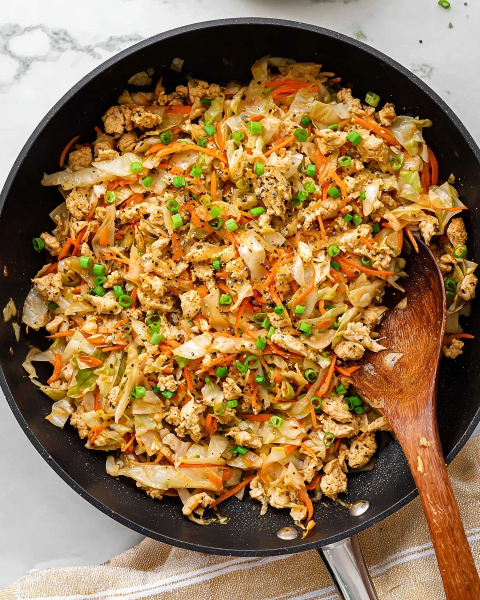 A close-up view of a black skillet filled with a mixed dish made of crumbled cooked chicken, thin orange carrot strips, and light beige cabbage pieces, all mixed well with black pepper seasoning and garnished with small bright green chopped scallions scattered on top; a wooden spoon is placed inside the skillet, partly covered by the food. The skillet rests on a white marbled surface with a folded beige and white striped cloth at the bottom edge. Photo taken with an iphone --ar 4:5 --v 7