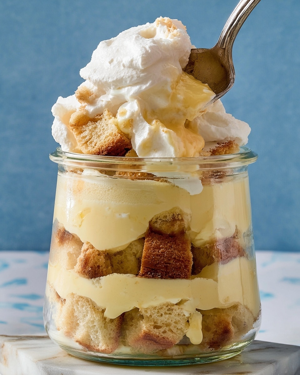 A clear glass jar shows multiple thick layers of dessert with a creamy light yellow custard filling alternating with chunks of light brown cake pieces. On top, there is a thick layer of white whipped cream draped over the jar’s rim, with a spoon partially scooping some of the dessert and cake pieces. The jar sits on a white marbled surface with a soft blue background. Photo taken with an iphone --ar 4:5 --v 7