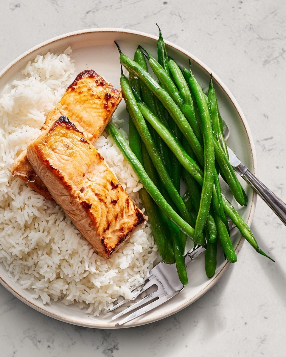 The dish shows a white round plate with three layers: at the bottom is a fluffy layer of white rice, topped with a browned, rectangular piece of cooked salmon with visible texture and slight char marks, located on the left side of the plate; next to the salmon, across the right and middle part of the plate, is a pile of bright green, whole green beans with smooth skins and rounded edges. A silver fork rests on the right side of the plate with its prongs touching the green beans. The plate is set on a white marbled texture surface. photo taken with an iphone --ar 4:5 --v 7