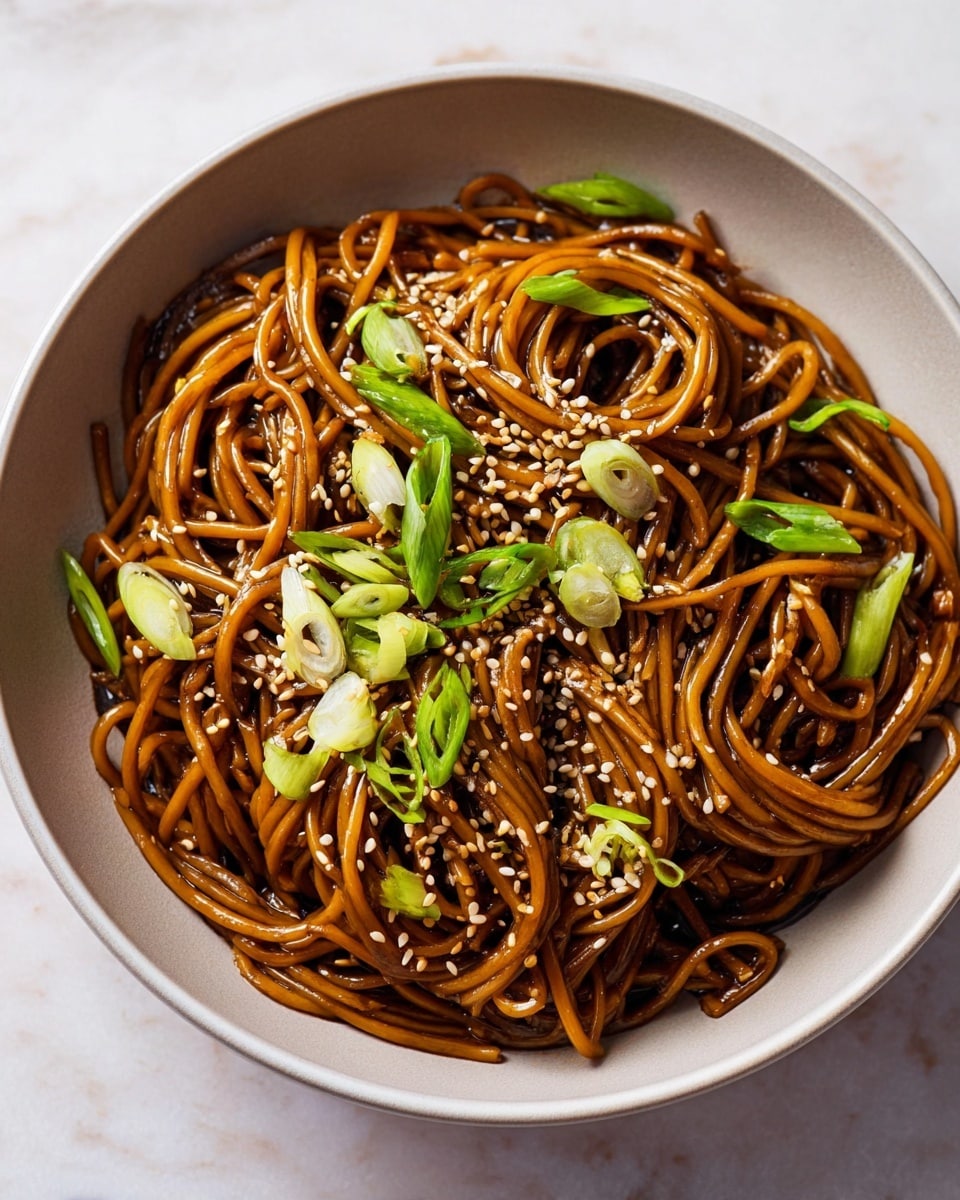 A bowl of dark brown stir-fried noodles sits on a white marbled surface. The noodles are shiny and intertwined in two main twisted piles, showing a smooth and slightly oily texture. Scattered on top are small, light beige sesame seeds and fresh green slices of spring onions that add brightness and contrast. The bowl holding the noodles is white with a smooth finish, enhancing the rich color of the noodles inside. Photo taken with an iphone --ar 4:5 --v 7