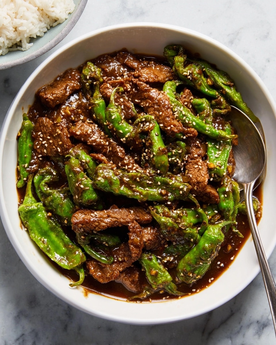A close-up of a white bowl filled with a stir-fry dish showing two main layers: bright green snap peas with a crisp texture and brown strips of cooked beef covered in a glossy, dark brown sauce. The pieces are mixed together, evenly coated with the sauce, and sprinkled with small black and white pepper flakes. A silver spoon rests inside the bowl on the right side, partially under the food. The bowl sits on a white marbled surface with part of another white bowl containing plain white rice visible in the top right corner. photo taken with an iphone --ar 4:5 --v 7