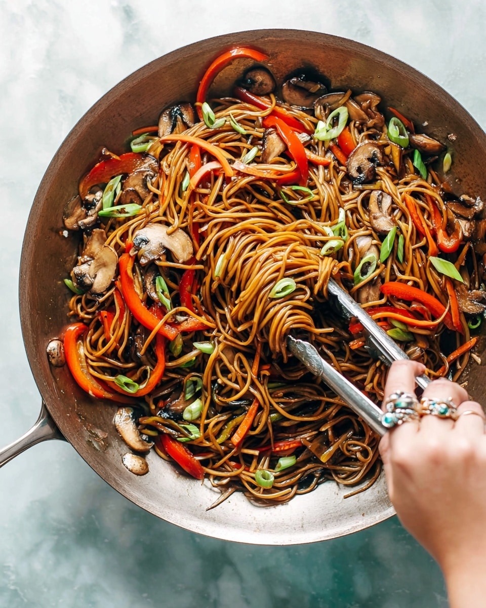 A close-up view of a pile of brown stir-fried noodles with a glossy texture, mixed with thin carrot strips in orange and small pieces of red bell pepper, as well as bits of green leafy vegetable. The noodles are lifted slightly by silver tongs, showing their soft and twisted shape. The food is inside a white pan with a shiny silver handle, and the background is a white marbled texture. photo taken with an iphone --ar 4:5 --v 7