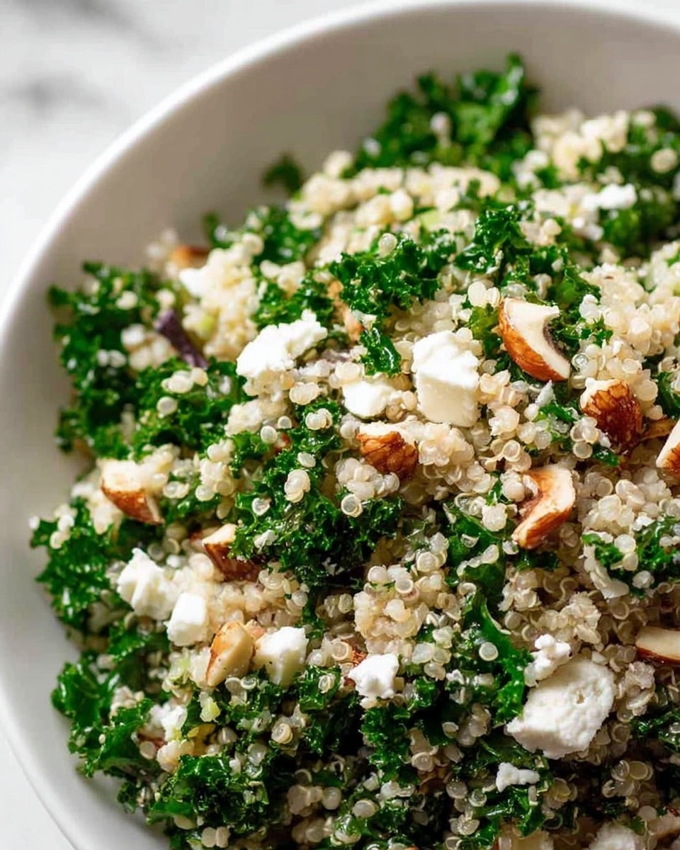 The image shows a close-up of a bowl filled with a layered quinoa salad. The base layer consists of white and slightly translucent cooked quinoa with small round grains. Mixed through the quinoa are bright green curly kale leaves, chopped finely. On top, there are small chunks of white cheese, scattered evenly, along with pieces of chopped nuts in light brown and beige tones. The bowl is white and placed on a white marbled surface. The textures of the quinoa grains look soft and fluffy, the kale leaves are crisp, the cheese is crumbly, and the nuts add a crunchy look. photo taken with an iphone --ar 4:5 --v 7