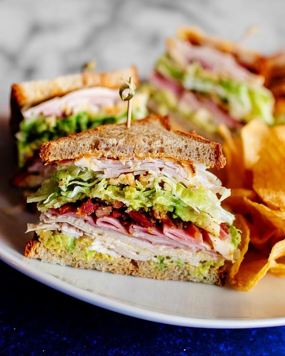 The image shows a club sandwich cut into a triangle and held together with a small toothpick, placed on a white plate with potato chips on the side. The sandwich has three layers of toasted brown bread with visible textures, layered with crispy green lettuce, slices of pink ham, white turkey meat, red bacon pieces, and a layer of green avocado spread. The sandwich looks thick and hearty, with each ingredient clearly stacked. The background is a white marbled surface. photo taken with an iphone --ar 4:5 --v 7