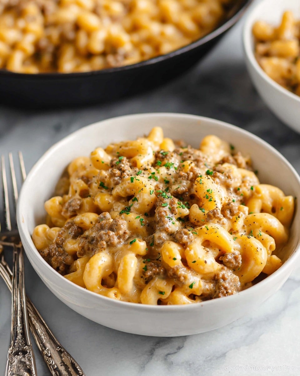 A white bowl filled with three layers of creamy macaroni and ground beef. The bottom layer is soft elbow macaroni pasta, the middle layer is browned ground beef mixed in, and the top layer is a thick, melted cheese sauce that coats the pasta and beef evenly. Small green parsley pieces and black pepper are sprinkled gently on top for color and texture. The bowl sits on a grey surface with two silver forks placed in front of it, and a cast iron pan filled with more of the same dish is blurry in the background. Photo taken with an iphone --ar 4:5 --v 7